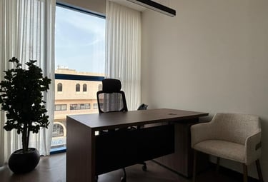 Modern office interior with a wooden executive desk, mesh chair, and large window with white curtains.