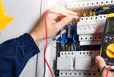 Professional electrician using a digital multimeter to test voltage in a residential circuit breaker panel.