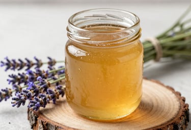 A 250ml glass jar of honey on a rustic wood slice, surrounded by wildflower lavender stems, soft natural side-lighting, elegant and gift-focused.