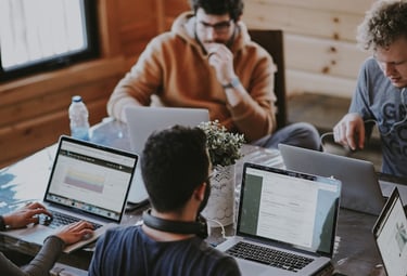 a group of people sitting around a table with laptops