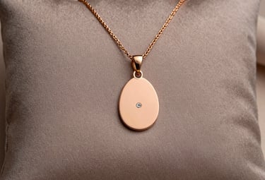 A minimalist photograph of a delicate rose gold pendant on a soft taupe silk cushion. The lighting is ethereal and soft, emphasizing the fine texture of the gold and the sparkle of a small inset diamond.