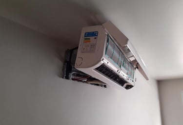 White split air conditioner unit mounted on a wall during maintenance with cover open.