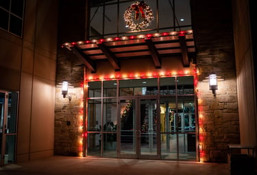 Modern office building entrance decorated with red Christmas lights and a lit holiday wreath at night.