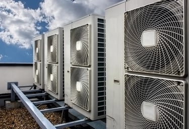 A row of industrial air conditioning units installed on a gravel rooftop under a blue sky.