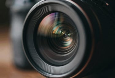 Artistic close-up of a lens reflection or camera detail in a dark, moody environment. Colors: #0D0D0D and subtle #6B705C highlights.