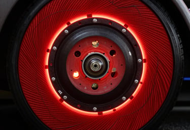 A close-up, high-speed photograph of a Formula 1 brake disc glowing intense racing red from heat during a night race. Sharp focus on the carbon fiber textures against a dark black background, professional motorsport cinematography, North American / US.