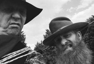 Black and white portrait of two rugged men in cowboy hats with long beards and western attire.
