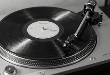 A sleek, black-and-white professional photograph of a vinyl record spinning on a modern turntable, emphasizing high-fashion minimalist aesthetics, North American / US music culture.