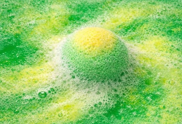 Oversized bath bomb releasing green and yellow foam with soft, creamy fizz.