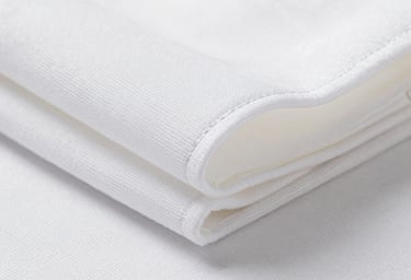 Close-up of tightly woven hospital-grade fabric — white polyester-cotton, visible tight weave structure under bright studio light, a folded stack showing clean seam lines, no people