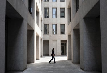 Candid street life photography in a clean, modern Western city, featuring a person walking through a shaft of light between tall buildings, high contrast, slate and light grey palette.
