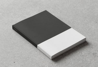 A minimalist artistic photograph of a single hand-bound publication resting on a stone surface, featuring colors #293B37 and #F1F4F2. Elegant, clean composition with soft side lighting.