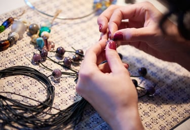 Manos artesanas ensartando cuentas de vidrio hechas a mano en un cordón negro para crear un collar.