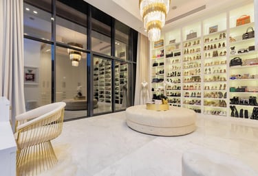 Luxurious walk-in closet with glass doors, shoe wall, and gold chandeliers.