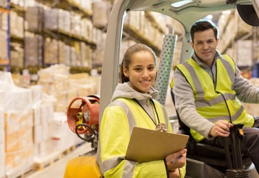 Trabajadores en un almacén usando chalecos reflectantes; uno manejando un montacargas y el otro con 
