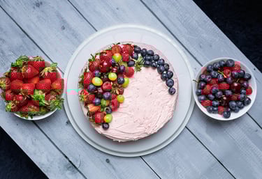 a cake with fruit on a table with bowls of fruit