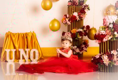 a baby girl in a red dress sitting on a floor
