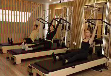 People doing Pilates exercise on tower reformers, pulling up the push-through bar in a studio