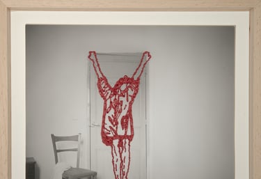 Conceptual art photo of a red beaded human figure hanging over a door in a minimalist room.