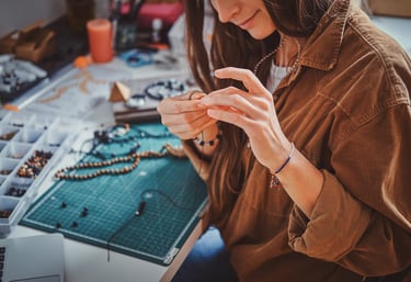 Artesano joyero elaborando un collar hecho a mano con cuentas en una mesa de trabajo.