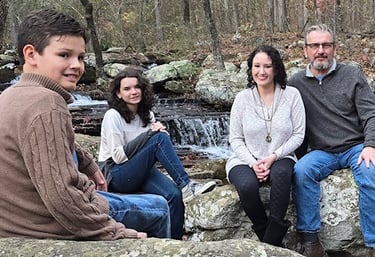 a family sitting on a rock formation in a wooded area