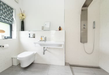 A modern, white bathroom showing a wall mounted sink and an electric shower. 