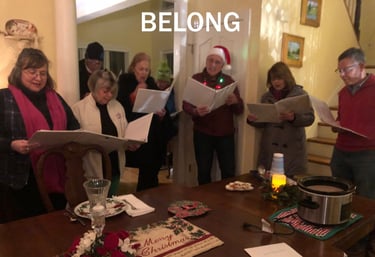 Group of seven adults singing Christmas carols around a table.