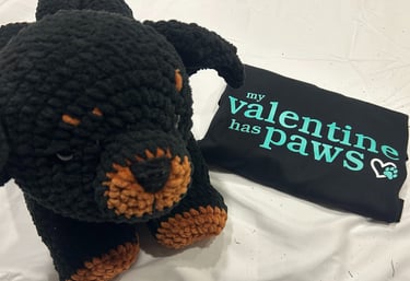 a folded tshirt that reads "my valentine has paws" sits beside a stuffed rottweiler