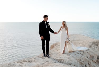 a bride and groom holding hands on a cliff