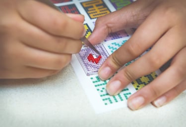 Human creating a picture by using tweezers, transparent baseplate and colorful pixel squares