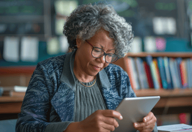a woman in glasses and a blue sweater is looking at a tablet computer