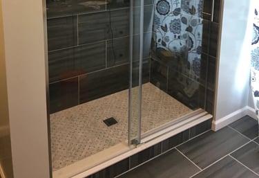 Modern walk-in shower with glass, dark gray tiles, light mosaic floor, stainless steel fixtures