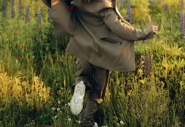 a woman in a coat and sneakers is running through the grass her left arm raised boldly