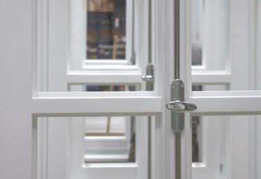 etailaufnahme weiß lackierter Holzfenster mit silbernem Griff und Blick durch mehrere Fensterebenen.