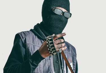 Studio photo of a man in a black jacket and a mask on, holding a belt