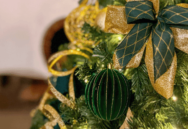 Uma árvore de Natal com um laço verde e dourado e uma bolinha verde