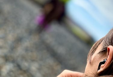 A woman wearing black wireless earbuds while jogging outdoors on a gravel trail.