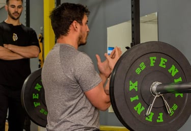 a man squatting on a barbEL WITH HIS PERSONAL TRAINER ON HIS SIDE