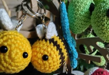 Llaveros de crochet amigurumi hechos a mano con abejas, pingüinos y hongos colgados en una exhibició