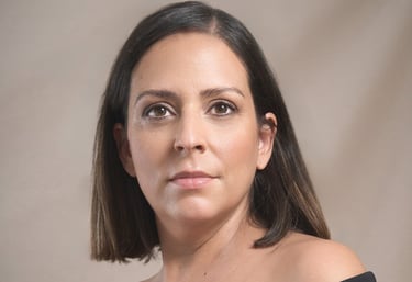 Professional headshot of a woman with dark hair wearing a black off-the-shoulder top.