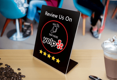 Yelp NFC review sign on cafe counter with coffee and beans. Boost feedback using digital tech.