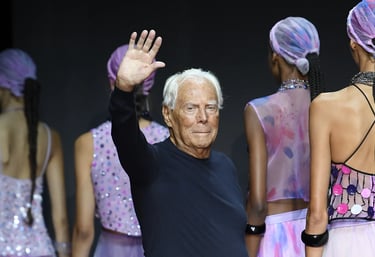 Giorgio Armani waves on the runway alongside models in colourful outfits.