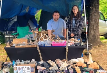 a man and woman standing in front of a vendor table with a variety of rocks and antlers