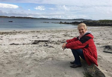 blonde haired woman sitting on a white sandy and rocky coastline bay