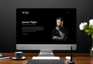 a computer screen on a desk featuring the homepage of a tattoo artist website