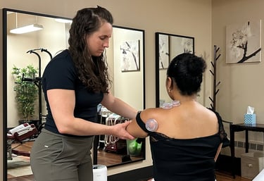 Chiropractor cupping a patient's shoulder and assisting movement with treatment room in background.