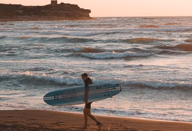 Surfer at sunset on Porto Ferro beach, Sassari, Sardinia, one of the island’s top surf spots.
