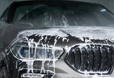 soapy front grill, lights and bumper of a grey bmw that is dripping wet with soap running down.