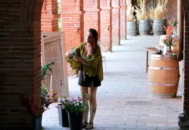 Estelle arrangeant des fleurs séchées dans des seaux sous une galerie en briques avec des arches