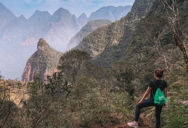 Uma pessoa de costas olhando para os vales no topo da montanha.